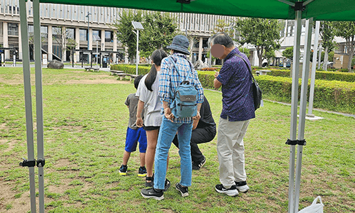 科学の祭典の会場で、親子がスタッフの案内でXR（AR）体験をしている様子