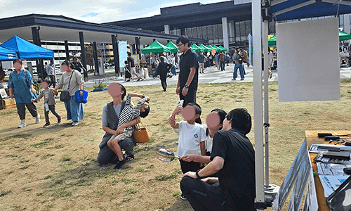 にこにこマルシェで、スタッフのサポートを受けながら親子がXR（AR）体験をしている様子