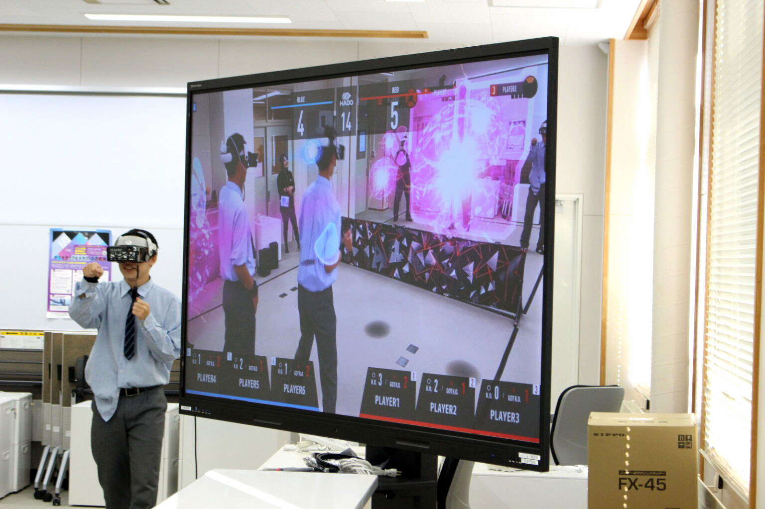 大型モニターにエナジーボールのエフェクトとスコアが映る試合風景。左で生徒がプレー中（HADO体験会）