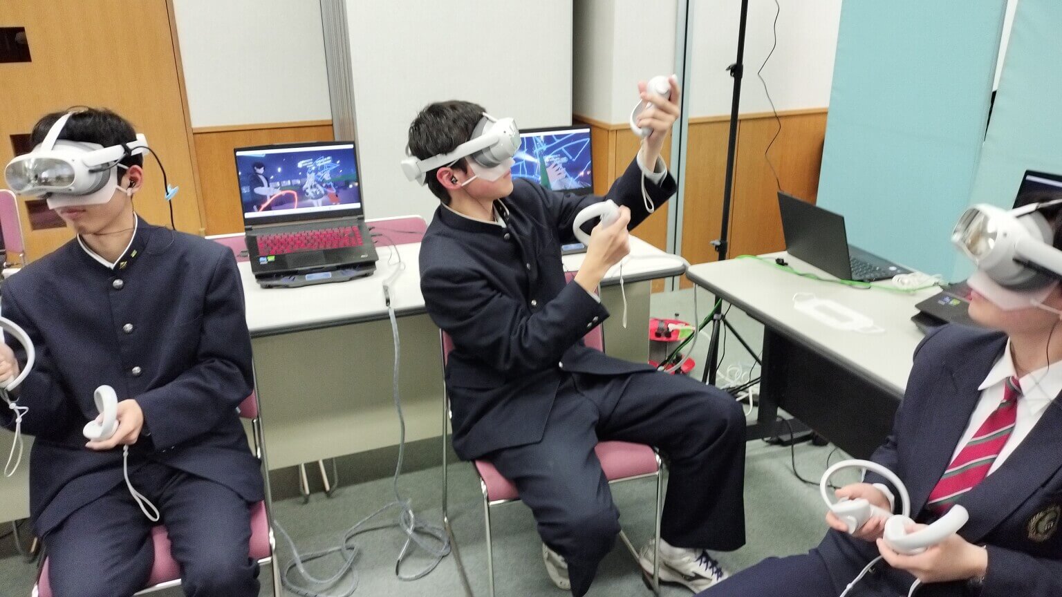 黒い学生服の生徒たちがVRゴーグルとコントローラーでアバターを操作するVRChat体験の場面